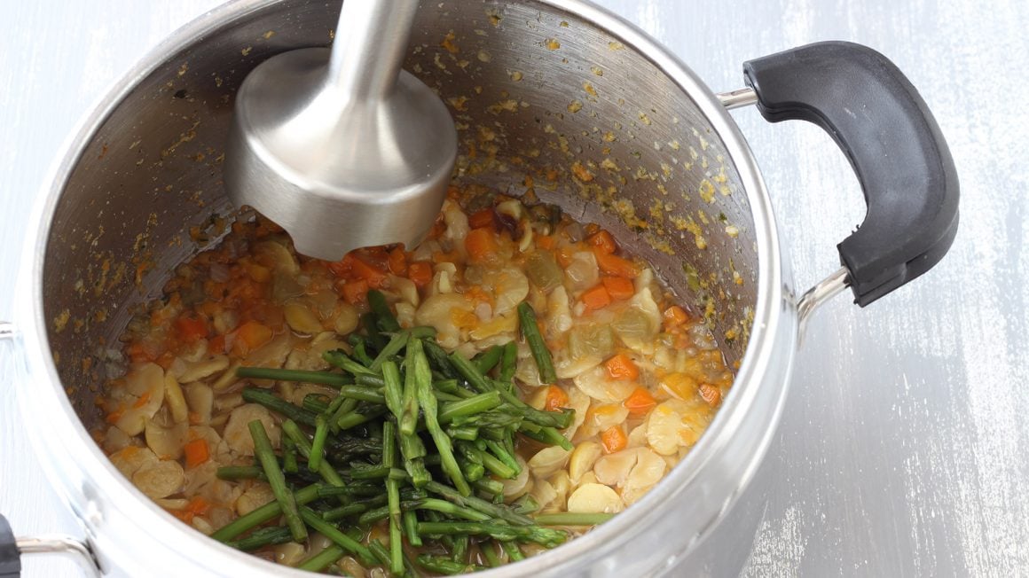 mixer a immersione che frulla le fave cotte con verdure e punte di asparago