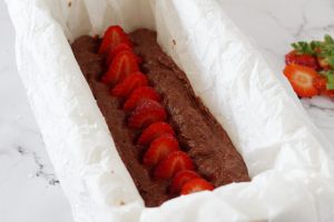 plumcake nello stampo pronto da cuocere con una fila di fragole in superficie