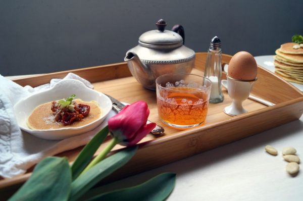 blini con pomodori su un vassoio con teiera, te e uovo alla coque