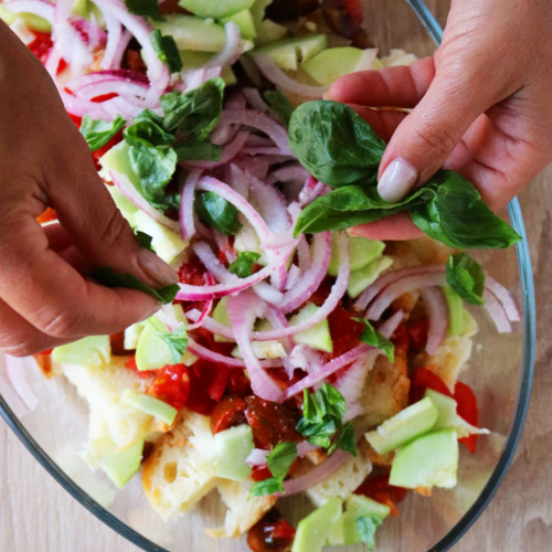 mani che aggiungono il basilico alla ciotola della panzanella