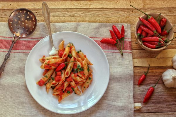 piatto di penne all'arrabbiata con ciotola di peperoncini e aglio