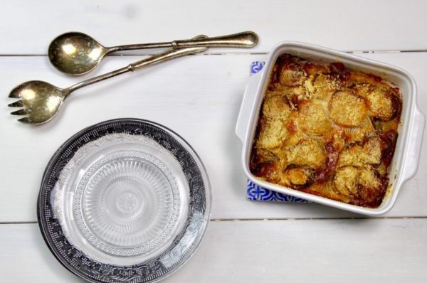 teglia di patate e cipolle gratinate su una tavola accanto a un piatto vuoto