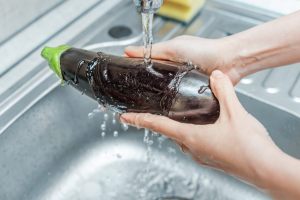 mani che lavano le melanzane sotto l'acqua