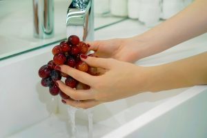 mani che lavano l'uva nera sotto l'acqua corrente