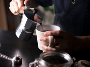 mani che versano il caffè in una tazza dalla moka