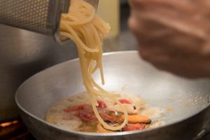 spaghetti versati nella padella con sugo di pomodorini e calamari
