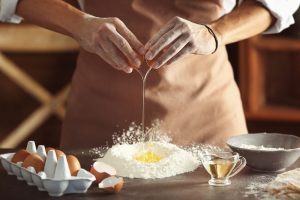 mani che versano le uova nella farina