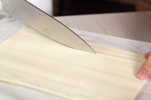 coltello che taglia una striscia da un rettangolo di pasta sfoglia